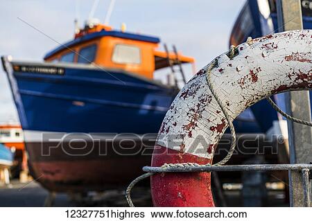 Stock Photograph - Close-up of a weathered life preserver and a fishing boat in the background; Seahouses, Northumberland, England. Fotosearch