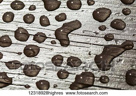 Stock Photograph - Close up of water droplets on stained wood, with small sun burst in water droplets; Calgary, Alberta, Canada. Fotosearch