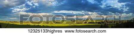 Stock Photograph - Clouds in a blue sky cast shadows on the lush, green fields below; Alberta, Canada. Fotosearch