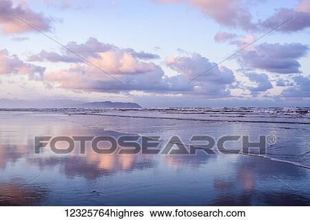 Stock Photograph - Clouds reflect on an Oregon beach at sunrise; Hammond, Oregon, United States of America. Fotosearch