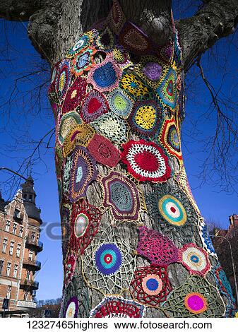 Stock Photograph - Colourful crocheted doilies on the trunk of a tree; Stockholm, Sweden. Fotosearch