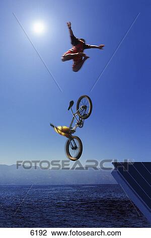 Stock Image - Cyclist going off jump into water. Fotosearch