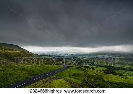 Stock Photograph - Dark storm clouds over a lush, green landscape and road; North Yorkshire, England. Fotosearch