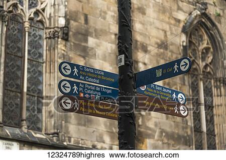 Stock Photograph - Destination signs for landmarks on a post with an old stone wall and windows in the background, Gothic Quarter; Barcelona, Catalonia, Spain. Fotosearch