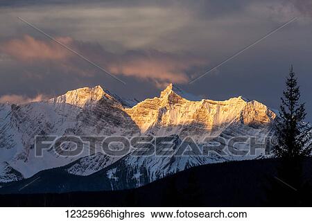 Dramatic glow on snow covered mountains at sunrise; Kananaskis Country, Alberta, Canada View Large Photo Image Stock Photograph - Dramatic glow on snow covered mountains at sunrise; Kananaskis Country, Alberta, Canada. Fotosearch
