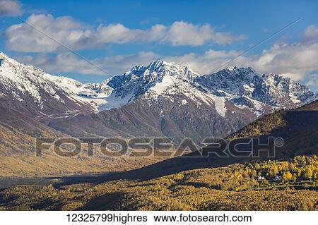 Stock Photograph - Eagle River Valley, homes nestled among the trees in the foreground, autumn coloured trees filling the valley, snow covering the Chugach Mountains in the background, Eagle River, South-central Alaska; Alaska, United States of America. Fotosearch