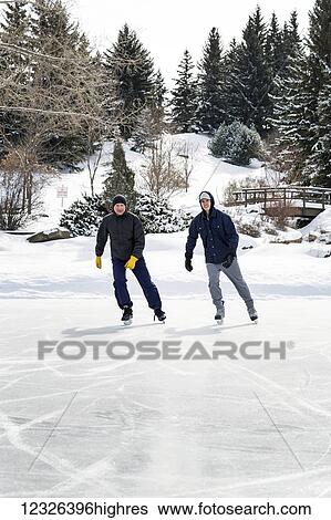 Father and son skating on pond with snow covered bridge in the background; Calgary, Alberta, Canada View Large Photo Image Stock Photograph - Father and son skating on pond with snow covered bridge in the background; Calgary, Alberta, Canada. Fotosearch