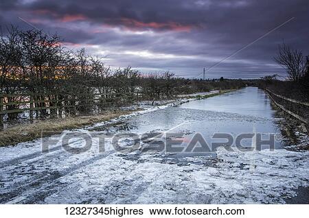 Stock Photograph - Flooded road with snow and water in winter at sunset; South Tyneside, Tyne and Wear, England. Fotosearch