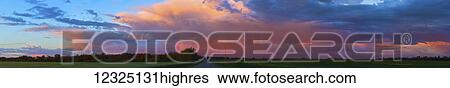 Stock Photograph - Glowing pink clouds over green fields and a country road at sunset; Alberta, Canada. Fotosearch