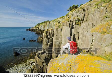 Stock Photograph - Hiker along basalt rock cliffs, Bay of Fundy; Brier Island, Nova Scotia, Canada. Fotosearch