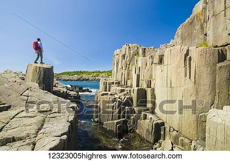 Stock Photograph - Hiker along basalt rock cliffs, Bay of Fundy; Brier Island, Nova Scotia, Canada. Fotosearch