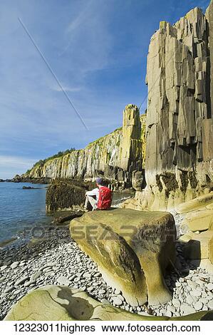 Stock Photograph - Hiker along basalt rock cliffs, Bay of Fundy; Brier Island, Nova Scotia, Canada. Fotosearch