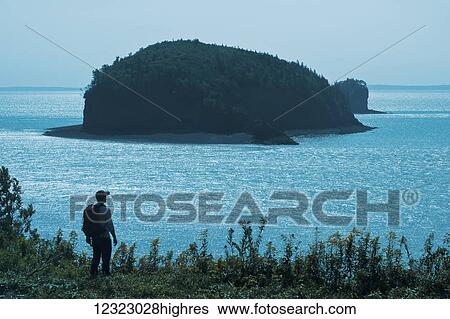 Stock Photograph - Hiker overlooking island, near Parrsboro, Minas Basin, Bay of Fundy; Nova Scotia, Canada. Fotosearch