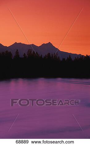 Stock Photo - Lake at sunset with trees and mountains in background. Fotosearch