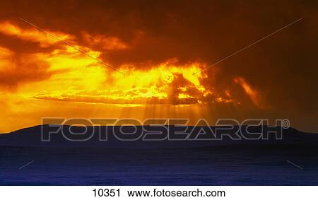 Stock Image - Light beams breaking through clouds at sunset. Fotosearch