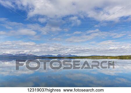 Stock Photograph - Light clouds reflect on the calm water of Tikchik Lake at the Tikchik Narrows Lodge, Wood Tikchik State Park, Southwestern Alaska; Alaska, United States of America. Fotosearch