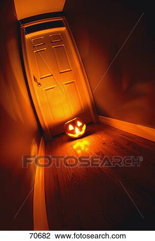 Stock Image - Lighted jack-o-lantern on floor in front of door. Fotosearch