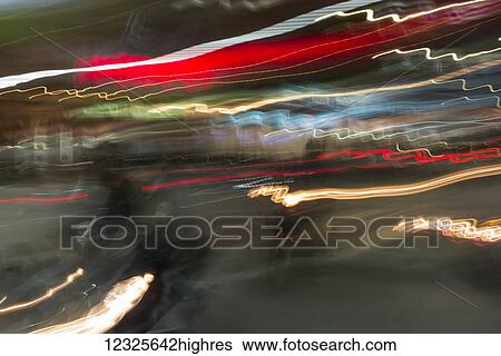 Stock Photograph - Long exposure of light trails in various colours and a faint view of a motorcycle on the street; Chiang Rai, Thailand. Fotosearch