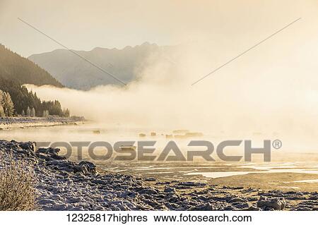 Stock Photograph - Low altitude fog is cast in warm sunset light along Turnagain Arm and the Seward Highway in winter, sea ice covering the ocean in the foreground, the Chugach Moutains revealed in the background, South-central Alaska; Alaska, United States of America. Fotosearch