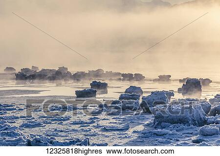 Stock Photograph - Low altitude fog is cast in warm sunset light along Turnagain Arm and the Seward Highway in winter, sea ice covering the ocean in the foreground, the Chugach Moutains revealed in the background, South-central Alaska; Alaska, United States of America. Fotosearch