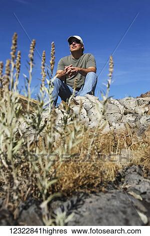 Low angle view of a man sitting on a rock ridge looking out; Oregon, United States of America View Large Photo Image Stock Photograph - Low angle view of a man sitting on a rock ridge looking out; Oregon, United States of America. Fotosearch