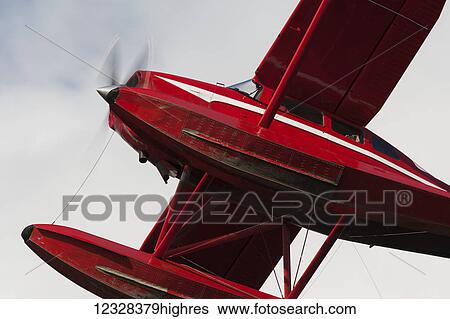 Stock Photograph - Low angle view of a red float plane against a cloudy sky; Alaska, United States of America. Fotosearch