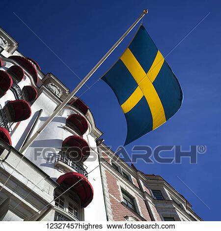 Stock Photograph - Low angle view of the Swedish flag and a building with red awnings over the windows, Ostermalm District; Stockholm, Sweden. Fotosearch