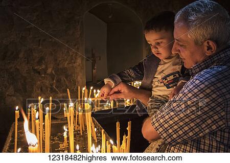 Stock Photograph - Man holding a boy lighting candles at Khor Virap Monastery; Ararat Province, Armenia. Fotosearch