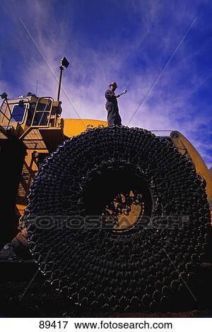 Man standing on chain-wrapped tire of ore hauler View Large Photo Image Stock Photo - Man standing on chain-wrapped tire of ore hauler. Fotosearch