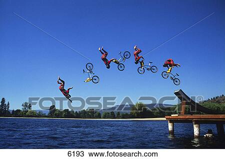 Stock Image - Multiple exposure of cyclist going off jump into water. Fotosearch