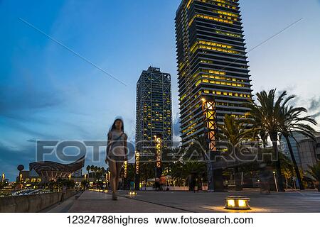 Stock Photograph - Olympic villa of Barcelona at sunset, a girl walking along the bund; Barcelona, Spain. Fotosearch