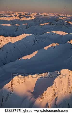Stock Photograph - Peaks of a snow covered mountain range glowing pink at sunset, Kachemak Bay State Park; Alaska, United States of America. Fotosearch