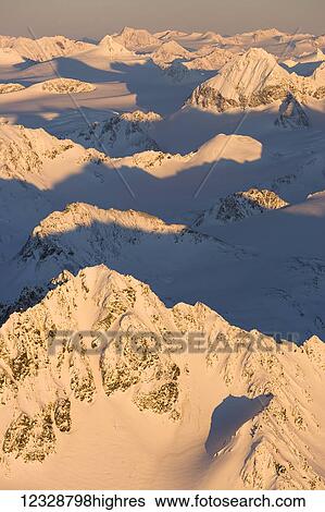 Stock Photograph - Peaks of a snow covered mountain range glowing pink at sunset, Kachemak Bay State Park; Alaska, United States of America. Fotosearch