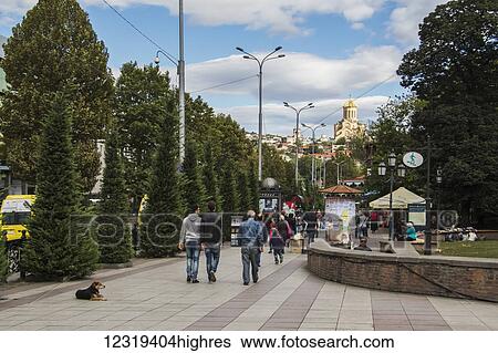 Stock Photograph - Pedestrians on Nikoloz Baratashvili Street, with Holy Trinity Cathedral of Tbilisi seen in the distance; Tbilisi, Georgia. Fotosearch