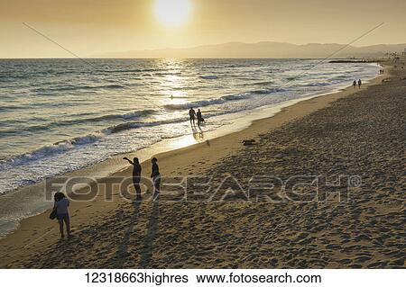 Stock Photograph - People stroll on Venice Beach at sunset; Venice Beach, California, United States of America. Fotosearch