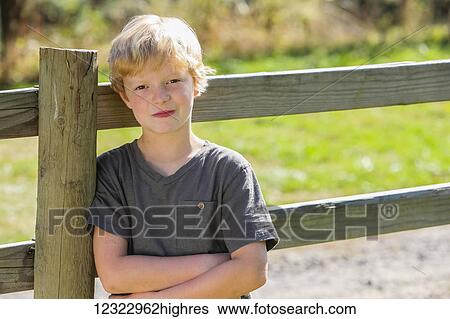 Portrait of a boy with blond hair leaning against a wooden rail fence; Oregon, United States of America View Large Photo Image Stock Photograph - Portrait of a boy with blond hair leaning against a wooden rail fence; Oregon, United States of America. Fotosearch