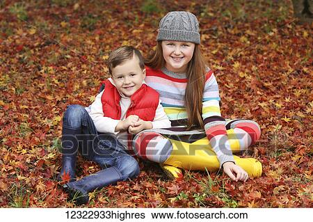 Stock Photograph - Portrait of a brother and sister sitting on the ground covered with fallen autumn coloured leaves; Oregon, United States of America. Fotosearch