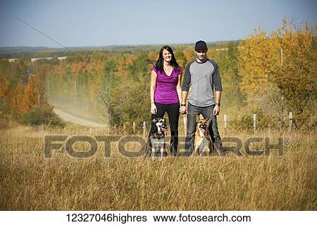 Stock Photograph - Portrait of a couple standing with their two dogs and an autumn coloured landscape in the background; Alberta, Canada. Fotosearch