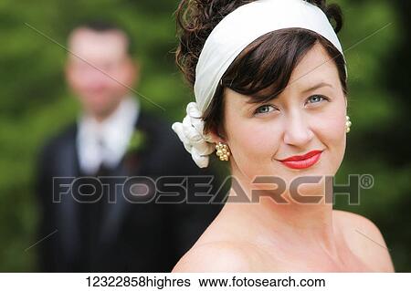 Portrait of a woman in a strapless dress and white headband with a man in a tuxedo blurred in the background; Oregon, United States of America View Large Photo Image Stock Photograph - Portrait of a woman in a strapless dress and white headband with a man in a tuxedo blurred in the background; Oregon, United States of America. Fotosearch