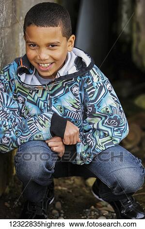 Stock Photograph - Portrait of a young boy crouching against a concrete wall; Oregon, United States of America. Fotosearch