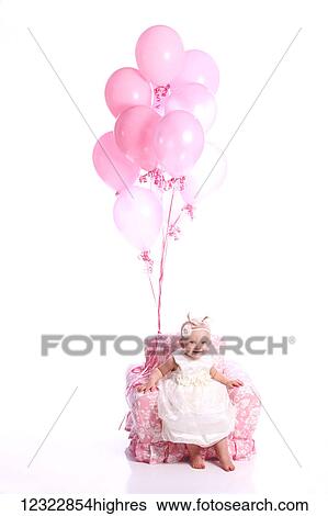 Stock Photograph - Portrait of a young girl in a white dress sitting in a pink chair with a bouquet of pink balloons; Oregon, United States of America. Fotosearch