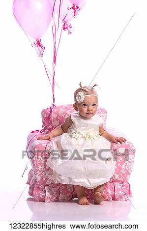 Stock Photograph - Portrait of a young girl in a white dress sitting in a pink chair with a bouquet of pink balloons; Oregon, United States of America. Fotosearch