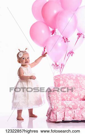 Stock Photograph - Portrait of a young girl with a pink chair and a bouquet of pink balloons. Fotosearch