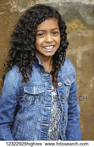 Stock Photograph - Portrait of a young girl with dark, curly hair and brown eyes standing against a concrete wall; Vancouver, Washington, United States of America. Fotosearch