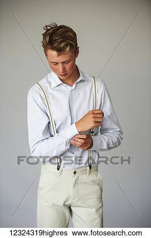 Stock Photograph - Portrait of a young man in a button up shirt and suspenders against a white background; Toronto, Ontario, Canada. Fotosearch