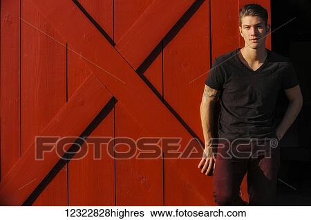 Stock Photograph - Portrait of a young man standing against a red barn door; Oregon, United States of America. Fotosearch