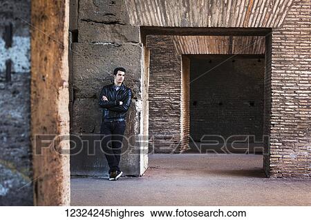 Stock Photograph - Portrait of a young man standing against a wall with concrete and brick facade; Rome, Italy. Fotosearch