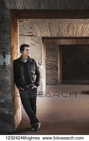Stock Photograph - Portrait of a young man standing against a wall with concrete facade; Rome, Italy. Fotosearch