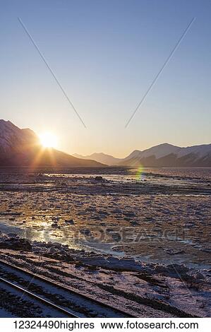 Railroad tracks lie in the foreground as sunrise peaks over Chugach Mountains lighting up an icy Turnagain Arm; Alaska, United States of America View Large Photo Image Stock Photograph - Railroad tracks lie in the foreground as sunrise peaks over Chugach Mountains lighting up an icy Turnagain Arm; Alaska, United States of America. Fotosearch