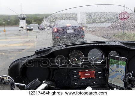 Stock Photograph - Raindrops cover the windshield of a cruiser motorcycle on the road; Englishtown, 0va Scotia, Canada. Fotosearch